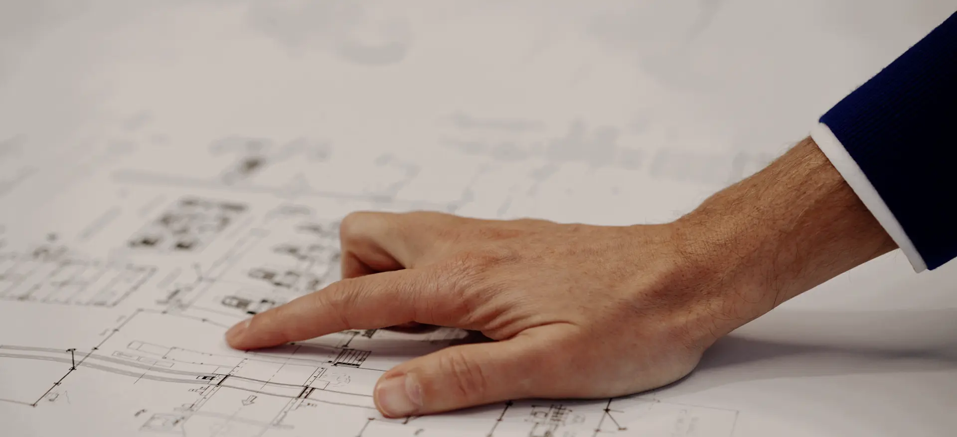 Primo piano su una mano di un uomo con la giacca e camicia che indica un disegno di una linea industriale