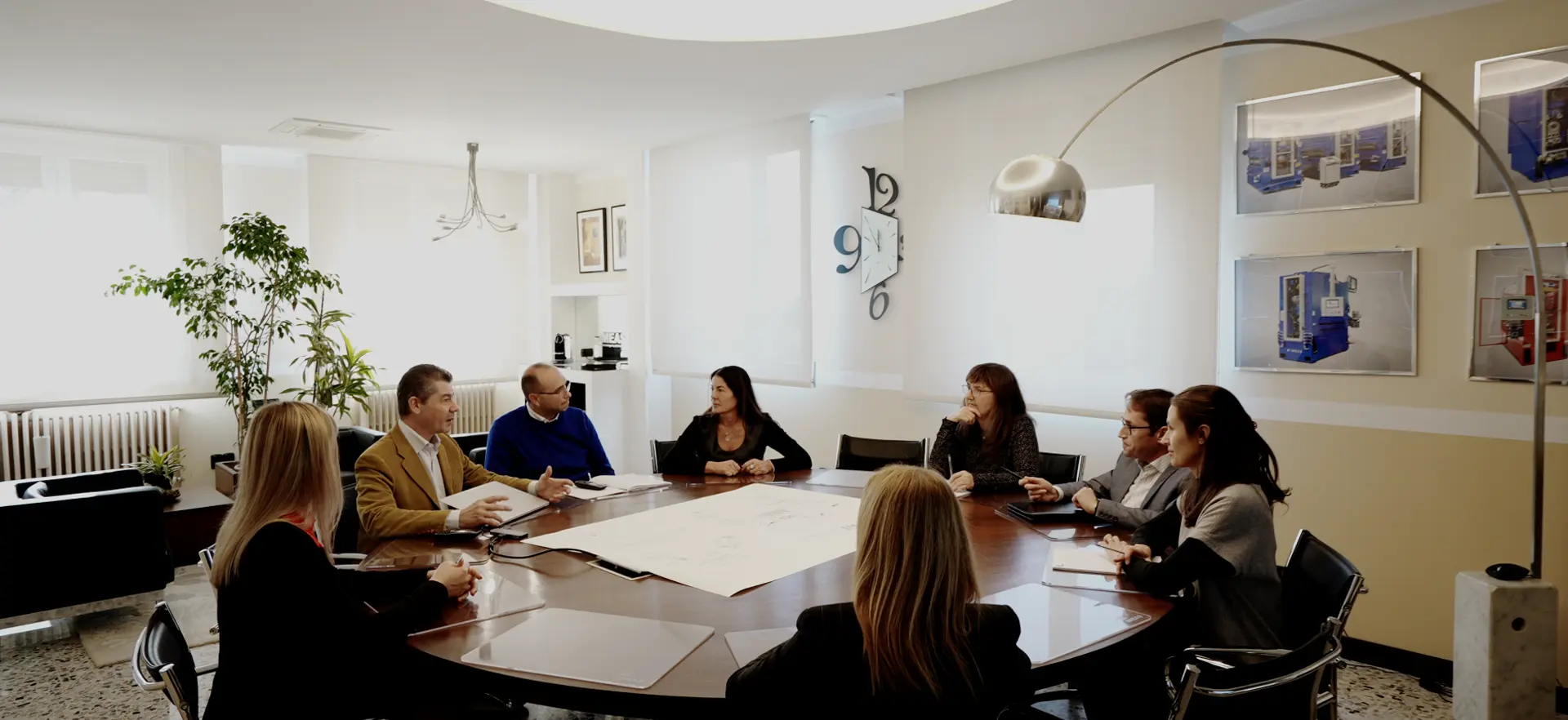 Riunione aziendale attorno a un grande tavolo con sei persone in una sala luminosa e moderna.