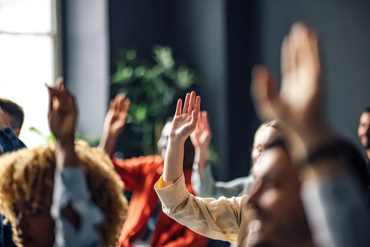 Persone che alzano la mano in un’aula o conferenza