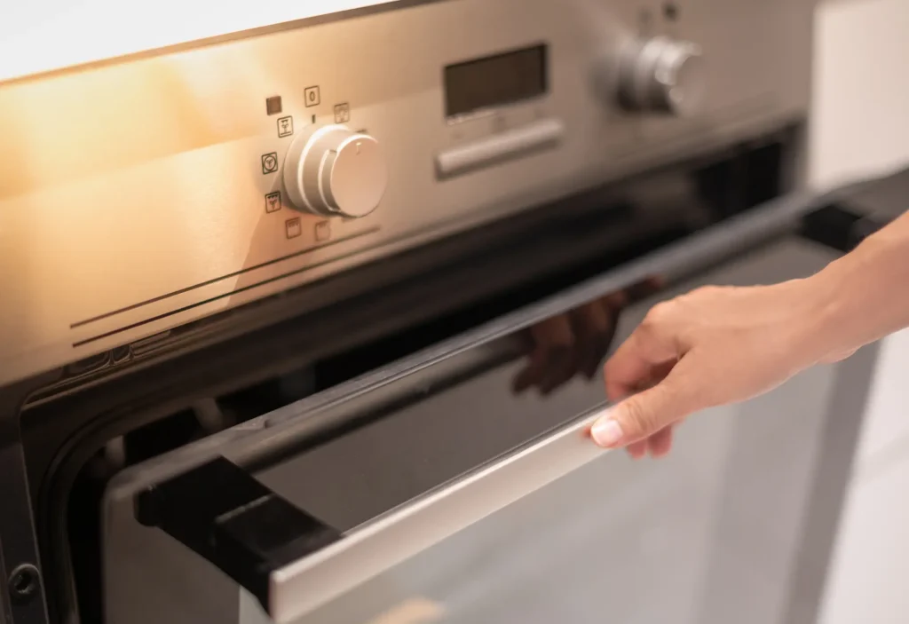 Mano che apre lo sportello di un forno da incasso in acciaio inox.