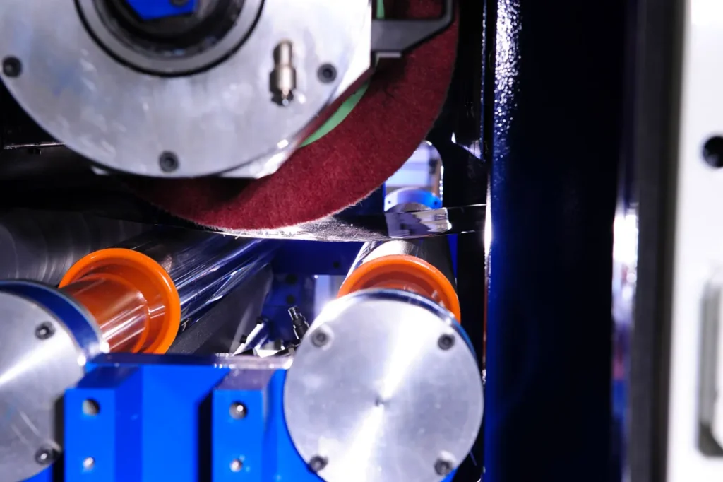 Macchina industriale che leviga un materiale con un nastro abrasivo rosso e rulli arancioni
